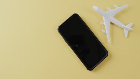 Close-up-of-white-plane-model,-smartphone-and-copy-space-on-yellow-background