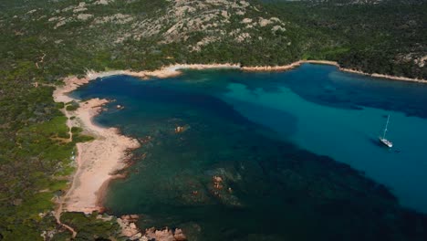 One-holiday-sailing-ship-boat-in-a-beautiful-Mediterranean-rock-beach-seaside-bay-with-crystal-clear-blue-turquoise-ocean-water-and-little-waves-in-Sardinia,-Italy