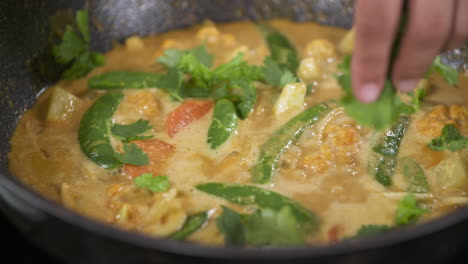 garnishing finishing coriander cilantro on vegan vegetarian yellow curry soup with vegetables green peas and carrots, thai food