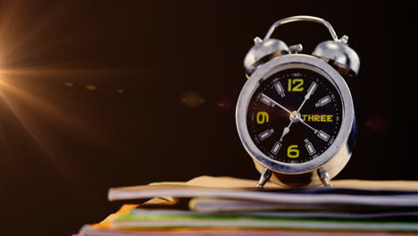 Animation-of-glowing-light-over-alarm-clock-on-stack-of-books