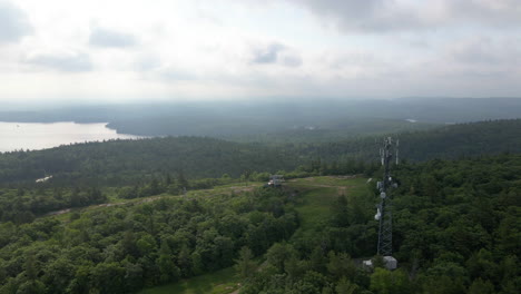 aerial footage above forest covered mountain with views of lake and radio tower on a cloudy day. calabogie ontario