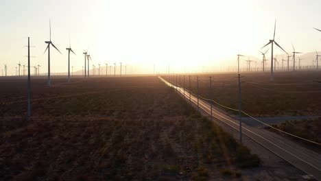 wind turbine farm with golden yellow sunset skies with view of empty road going off into horizon in the mojave desert