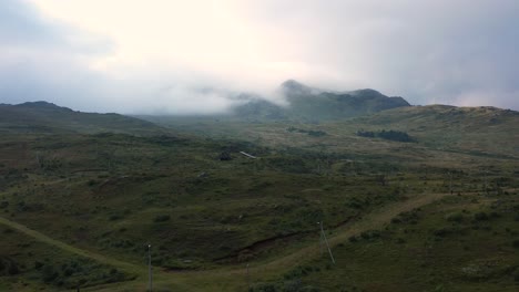 Flying-over-dirt-crossroads-in-the-countryside-of-Norway-into-a-spooky-and-moody-valley-with-foggy-mountains-in-the-distance