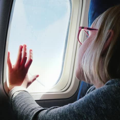 una niña de 6 años con anteojos se sienta en un avión mirando por la ventana