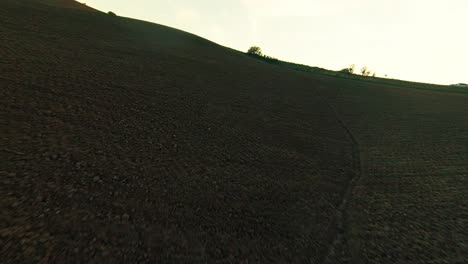 FPV-Drohne-über-Hügeliger-Landschaft-In-Richtung-Eines-Autos,-Das-In-Der-Abenddämmerung-Im-Gelände-In-Der-Nähe-Von-Pienza-In-Der-Toskana,-Italien,-Fährt