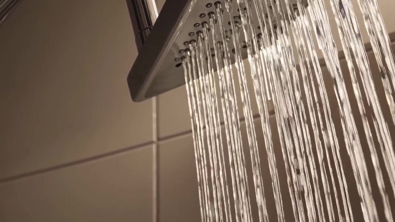 Primo piano dell'acqua che scorre da un soffione doccia moderno.