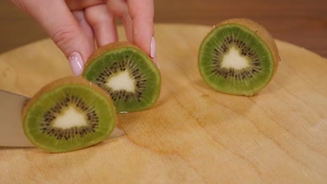 primer plano de una mujer cortando un kiwi fresco maduro con un cuchillo en una tabla de madera.