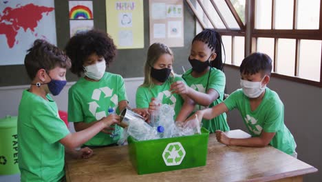 group of kids wearing face masks putting plastic items in recycle container