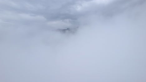 drone passing through white static high clouds where mountain range appears on the horizon