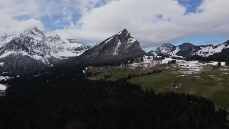 Aerial-perspective-of-the-Swiss-Alps-with-snow-capped-mountain-peaks-and-scattered-houses-nestled-amidst-the-landscape,-situated-near-Glarus,-Switzerland