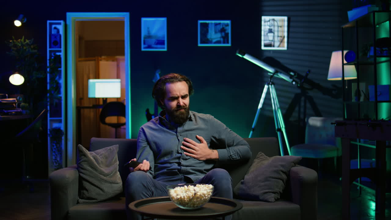 hombre sedentario en un apartamento sufriendo un ataque al corazón mientras ve la televisión