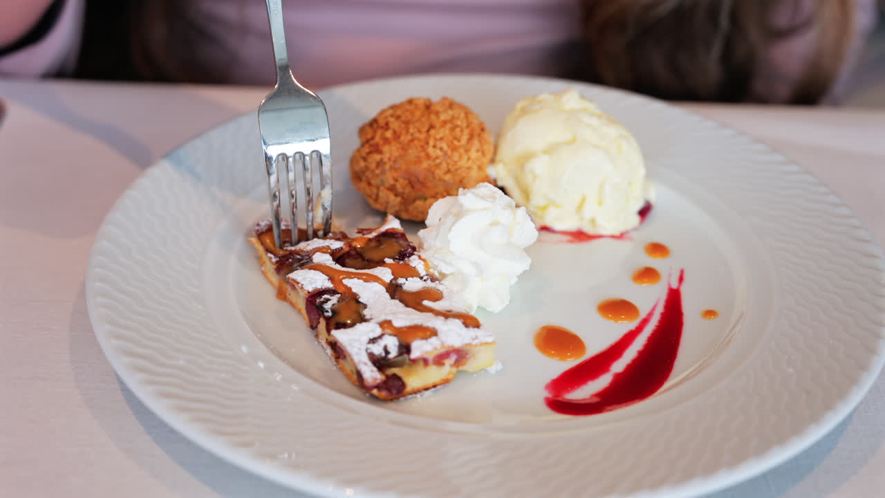 Close up of a woman eating dessert plate with a tart, a cream puff, ice cream, and sauces