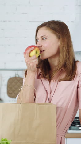 the girl in the kitchen takes out an orange and an apple from a paper bag. vegetarian food. vertical video
