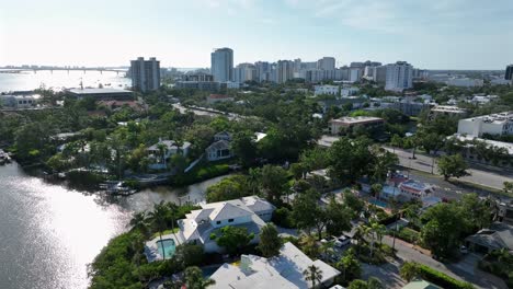 luxury villas at river bay with private access in sarasota city, florida. sunny day with downtown skyline in background. aerial wide shot. sun reflection on water surface at sunrise.