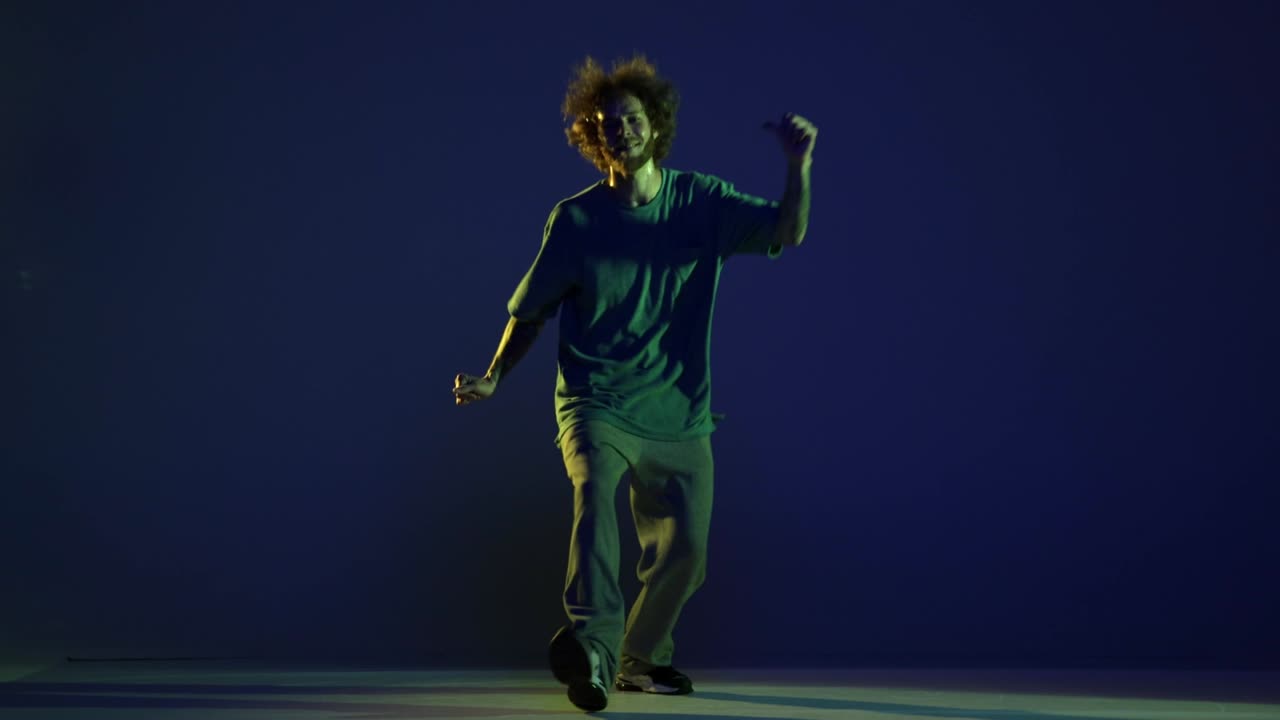 Emotional young man, hip-hop dancer dancing isolated over dark blue background in neon light. Modern dance art, fashion, youth, ad, style. 4K, video