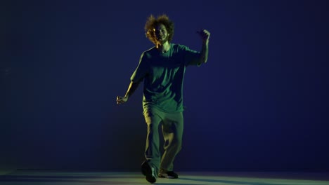 emotional young man, hip-hop dancer dancing isolated over dark blue background in neon light. modern dance art, fashion, youth, ad, style. 4k, video
