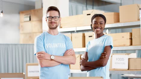 Caucasian-man-and-young-African-American-female-volunteer-standing-in-warehouse-looking-at-camera-and-smiling-in-good-mood