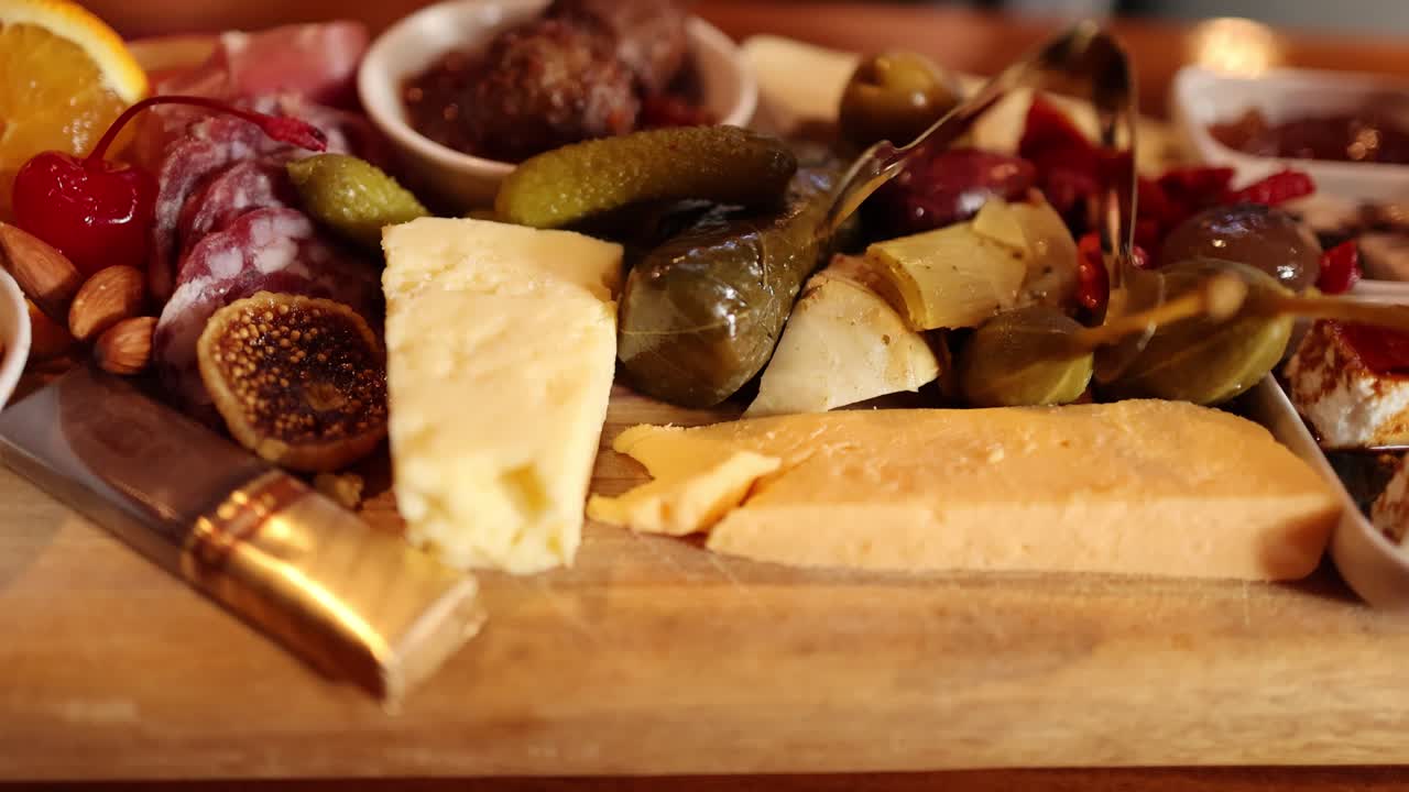 Charcuterie board with cheese, pickles, meats, and appetizers, shot in warm, rotating close-up
