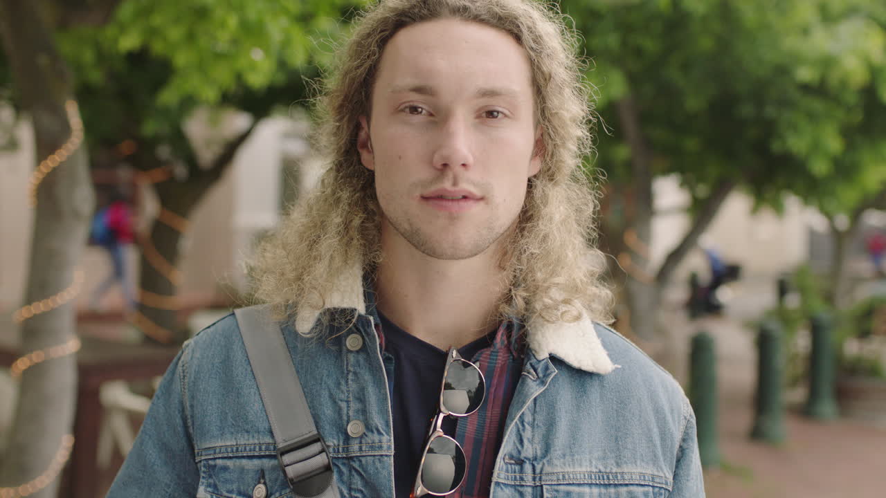 retrato de un atractivo joven estudiante rubio que mira en serio a la cámara confiado vistiendo moda de denim fresco en la calle de la ciudad urbana