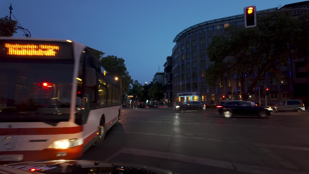 A local bus makes a turn on a bustling Berlin street at night, surrounded by cars and urban city lights.