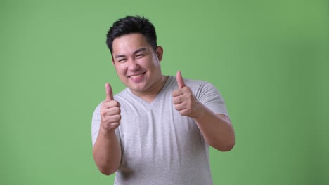 young handsome overweight asian man against green background