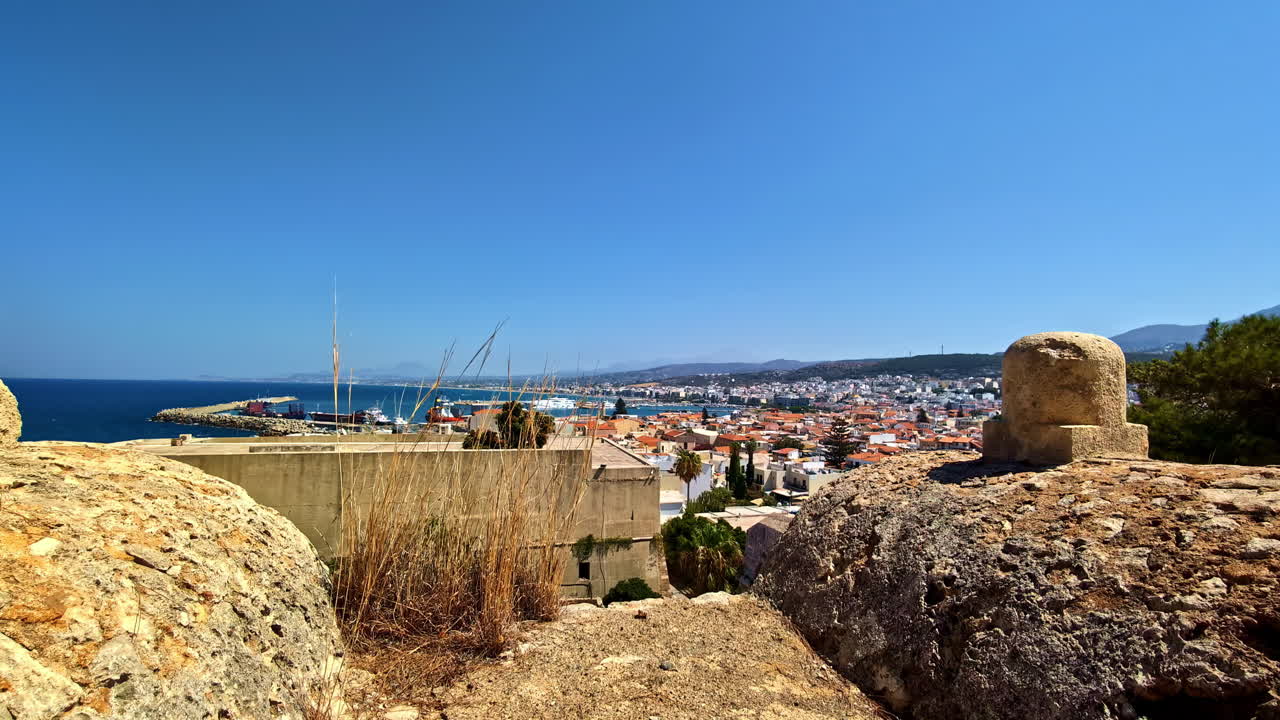 Vista elevada desde antiguas murallas de piedra con vistas a la ciudad costera y al mar azul cerca de la Fortezza Veneciana, Creta, Grecia