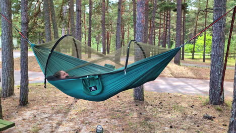 una persona relajándose en una hamaca colgada entre dos árboles en un campamento entre árboles altos en un bosque