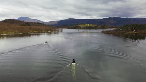 ángulo aéreo cinematográfico del sobrevuelo de drones siguiendo a tres barcos que se acercan a los estrechos en loch lomond en escocia