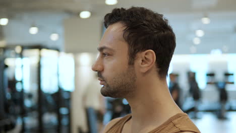 face close-up of thoughtful sporty bearded man standing in modern gym - parallax slow motion