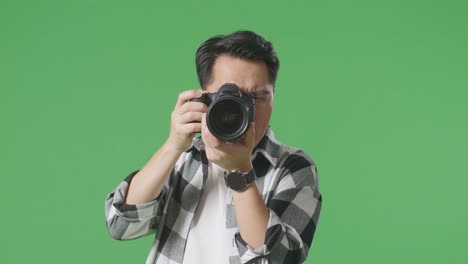 close up of asian photographer having a neck ache after using a camera taking some pictures while standing on green screen background in the studio