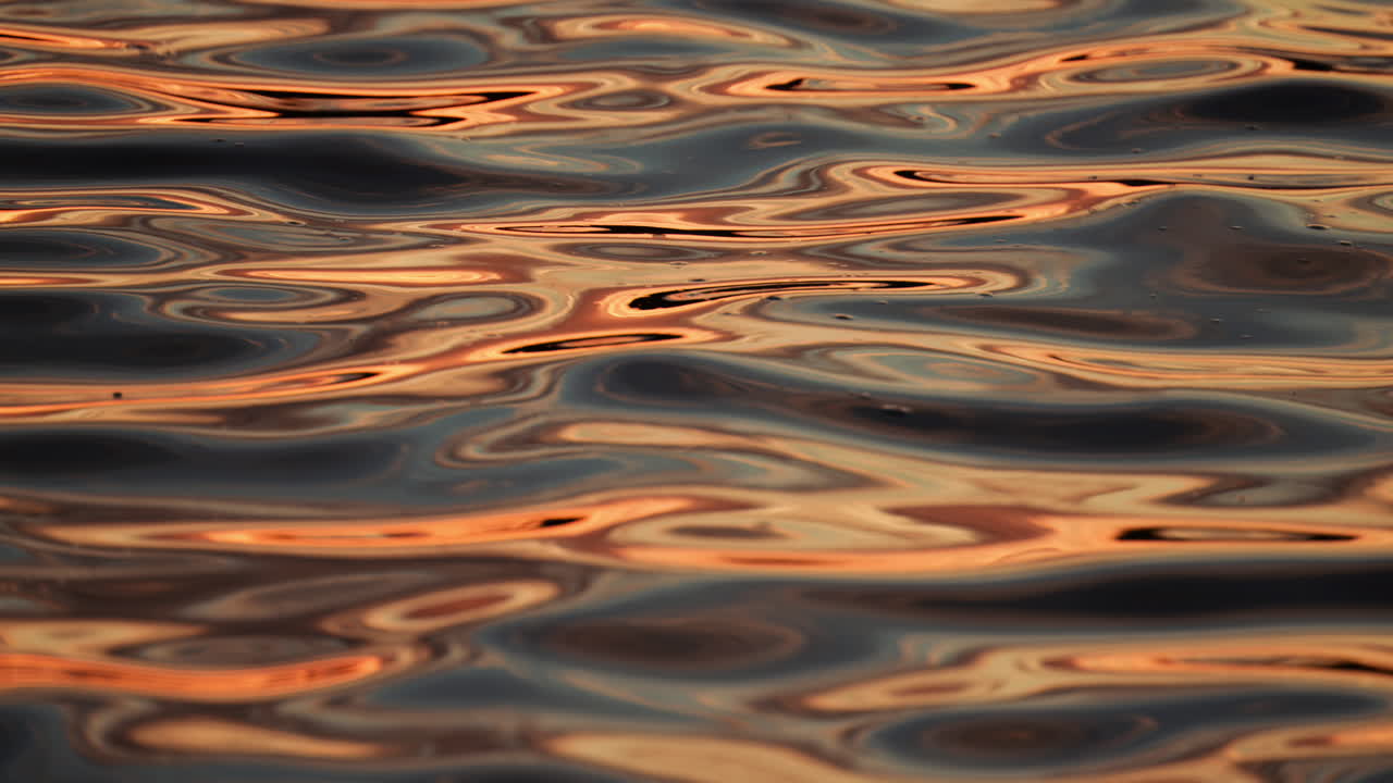 Golden sunlight dances on the calm water's surface, creating beautiful reflections at dusk. Slow motion reflection of sunset on water waves