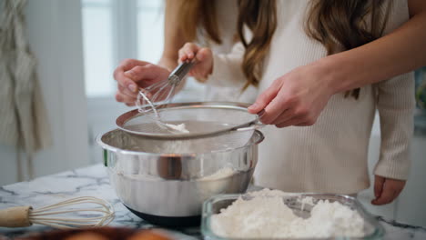 mother daughter hands sifting flour home closeup. unknown family cooking pastry