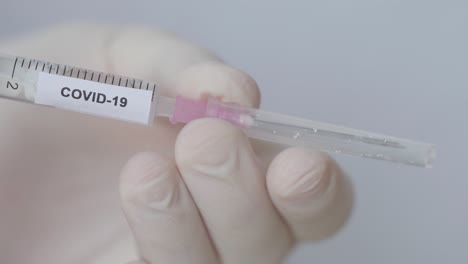 attaching hypodermic needle with plastic cap to syringe with fluid and covid-19 label - close up