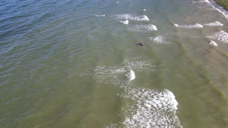 Person-on-a-stand-up-paddle-board-lays-down-and-starts-paddling-through-the-waves-at-Bonniebrook-beach-in-Gibsons,-Canada