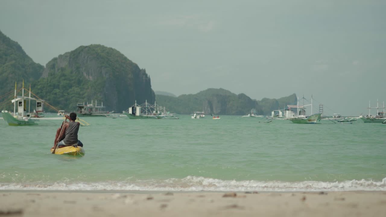 엘 니도의 해안선 근처에서 보트를 향해 노를 젓는 카약을 공유하는 두 사람