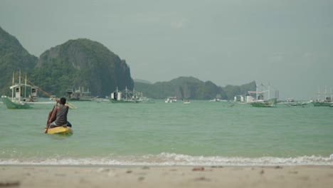 dos personas compartiendo un kayak remando hacia un bote cerca de la costa en el nido
