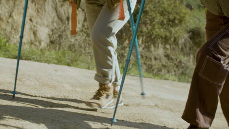 close up of two unrecognizable hikers with trekking poles walking up hill on a sunny day