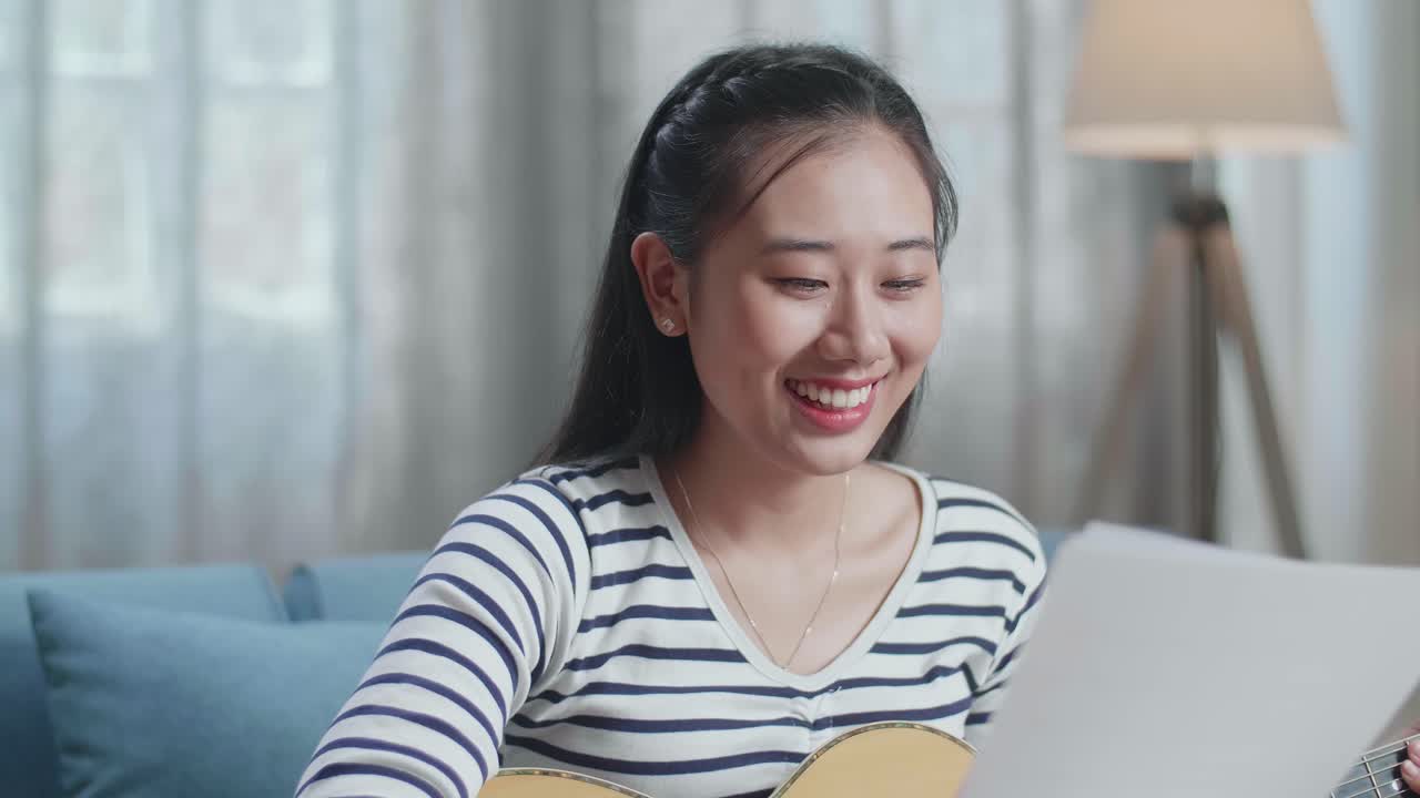 집에서 기타를 연주하기 전에 종이를 들고 있는 아시아 여성 작곡가의 클로즈업