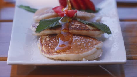 a female hand pouring maple syrup on a dish with many pancakes for breakfast