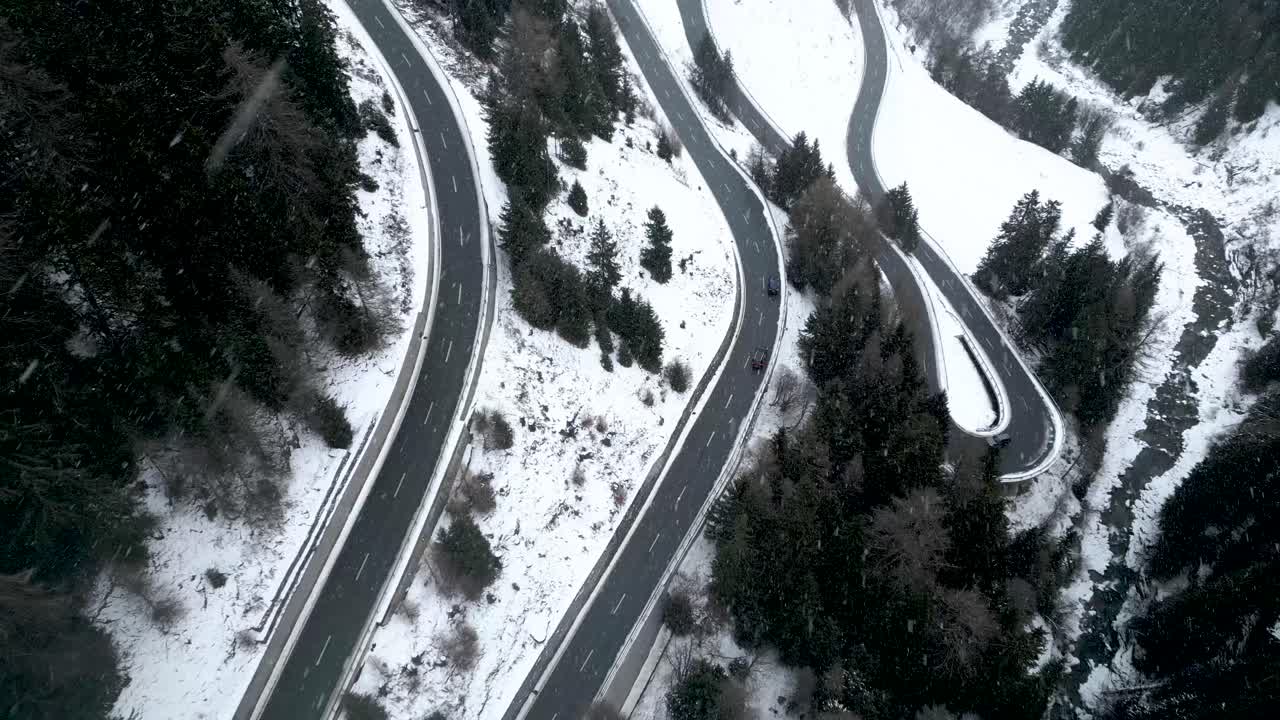 Aerial view of a small car driving on a snow covered mountain road during a cloudy winter day with snowfall in Switzerland
