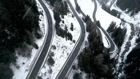 vista aérea de un coche pequeño conduciendo por una carretera de montaña cubierta de nieve durante un día nublado de invierno con nevadas en suiza