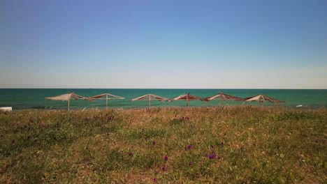 Sonnenschirme-Lugen-Hinter-Einem-Grasbewachsenen-Hügel-Vor-Dem-Hintergrund-Des-Blauen-Himmels-Und-Des-Meeres-Hervor