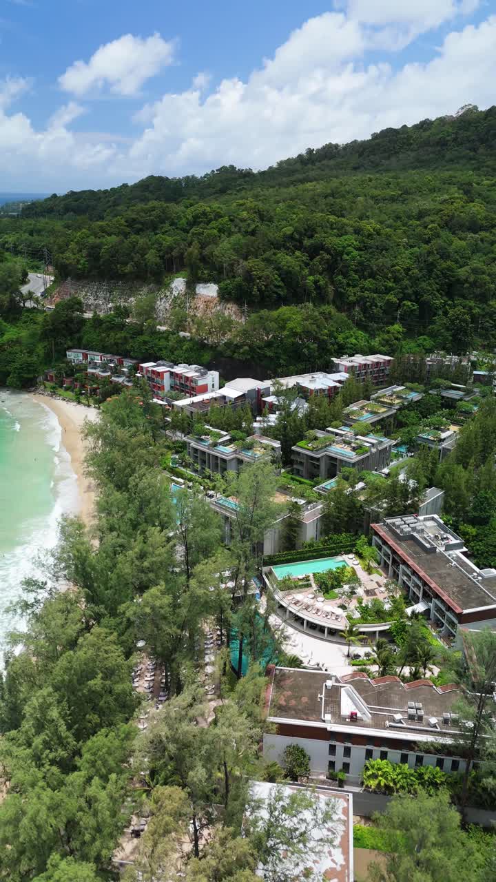 Vertical aerial pan shows luxury resorts and turquoise Kamala Beach, Phuket