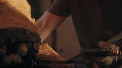 close up of welding work with sparks and gloves near a clay structure in dim light