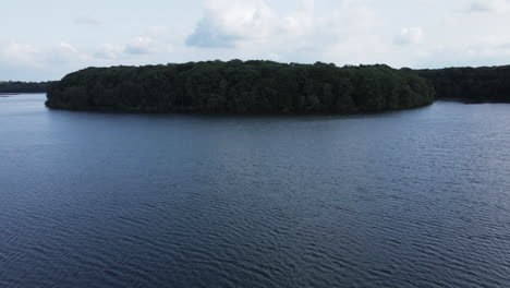 Flying-over-Trémelin-or-Tremelin-lake-at-low-altitude-over-rippled-water-surface,-Brittany-in-France