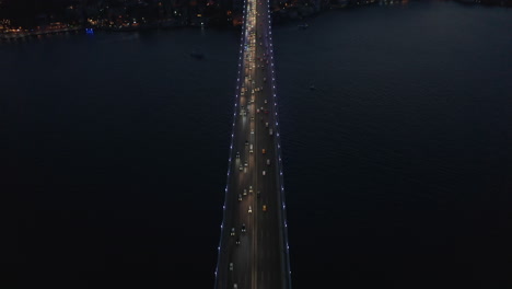 Birds-Eye-Top-Down-View-of-Bridge-at-Night-with-Car-traffic-looking-up-revealing-City-Skyline-Silhouette,-Aerial-tilt-up