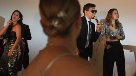 clip of an elegant party where women in formal dresses enjoy live music. a band can be seen livening up the event.