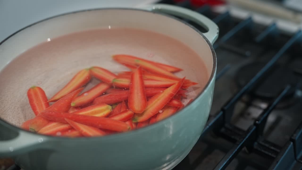 Brightly colored carrots boiling on the stove top (slow motion, 4K)