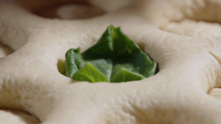 Bringing fingertip placing small green leaf into risen dough dimple at kitchen prep for baking