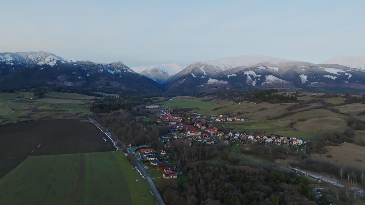 vuela sobre un pequeño pueblo con casas y montañas cubiertas de nieve en el fondo
